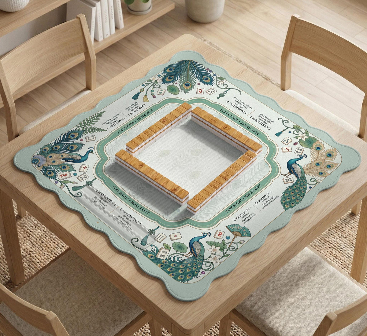Teal square mahjong mat with peacock feathers, soft floral pattern, tassel details, and printed rule guide text in the center.