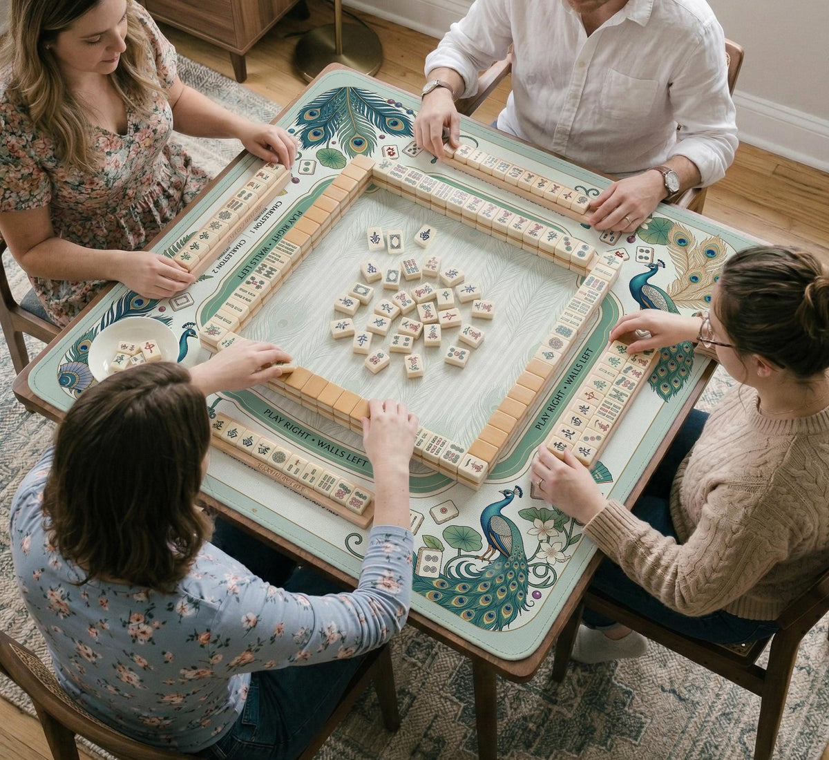 Teal square mahjong mat with peacock feathers, soft floral pattern, tassel details, and printed rule guide text in the center.