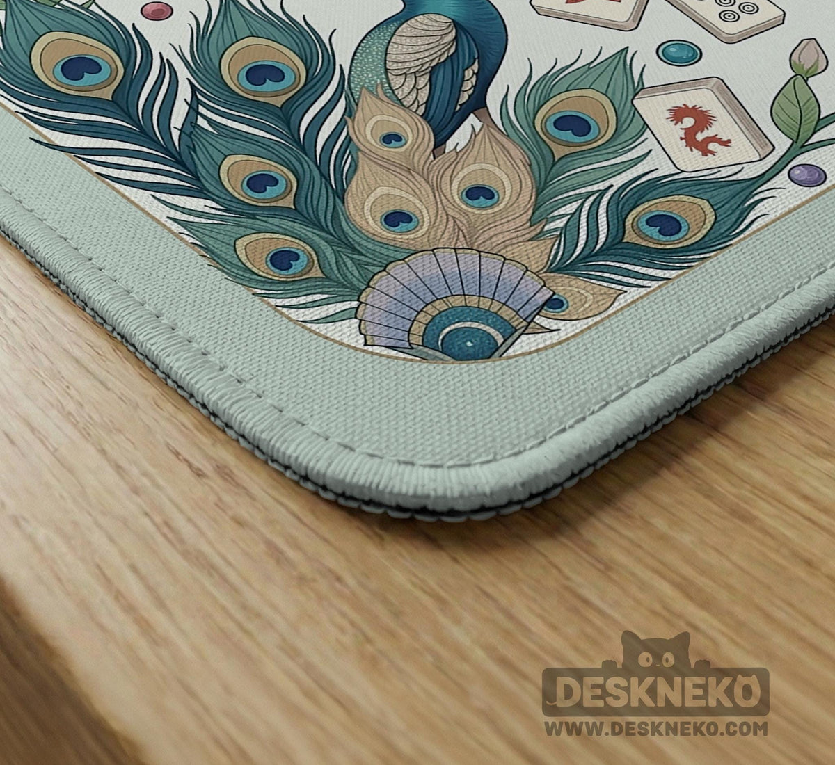 Teal square mahjong mat with peacock feathers, soft floral pattern, tassel details, and printed rule guide text in the center.