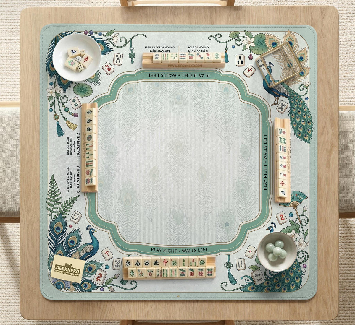 Teal square mahjong mat with peacock feathers, soft floral pattern, tassel details, and printed rule guide text in the center.