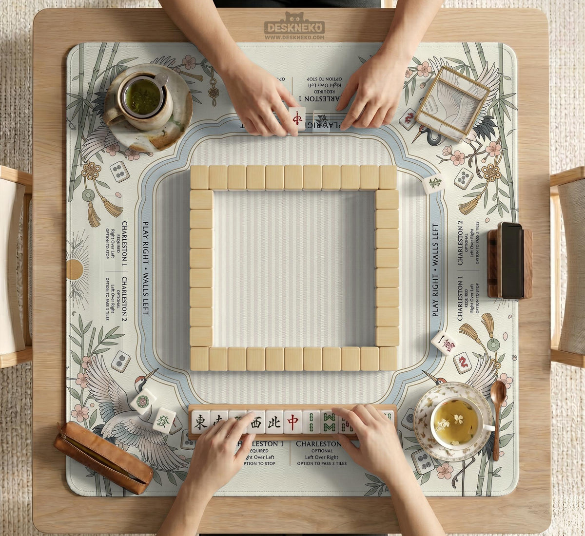 Beige square mahjong mat with a sage border, crane birds, bamboo, flowers, tile icons, and printed rules around a clean center play area.