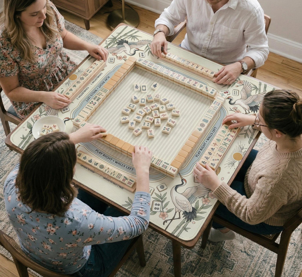 Beige square mahjong mat with a sage border, crane birds, bamboo, flowers, tile icons, and printed rules around a clean center play area.