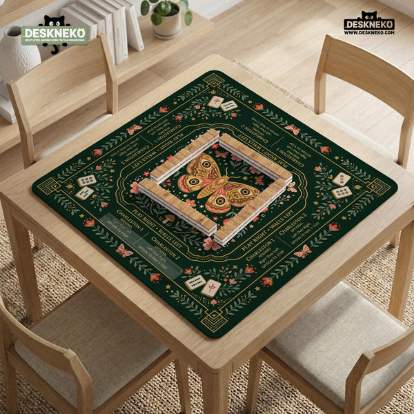 Dark botanical mahjong table mat with a floral border, large moth and butterfly design in the center, gold corner frame, and printed rules layout around the edge.