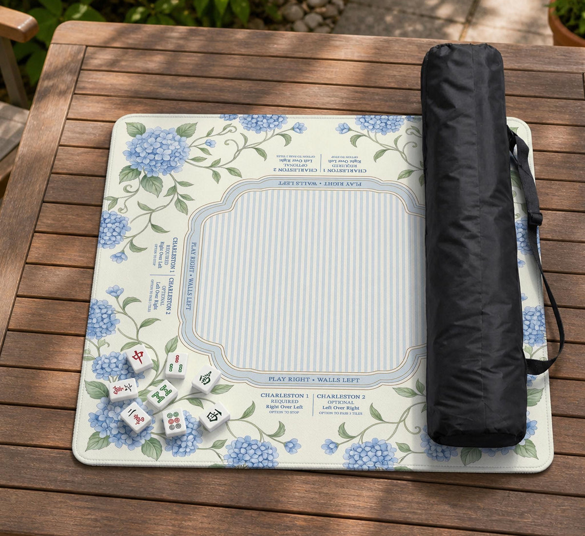 A square mahjong mat with blue hydrangea flowers, green vines, a cream background, a striped center, and printed rules around the border.