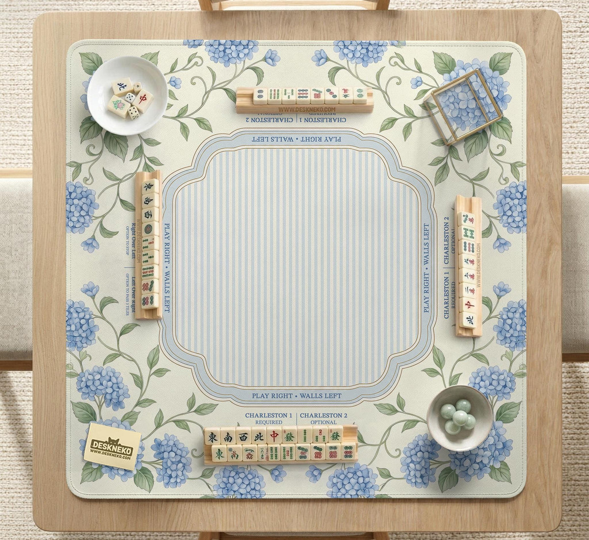 A square mahjong mat with blue hydrangea flowers, green vines, a cream background, a striped center, and printed rules around the border.