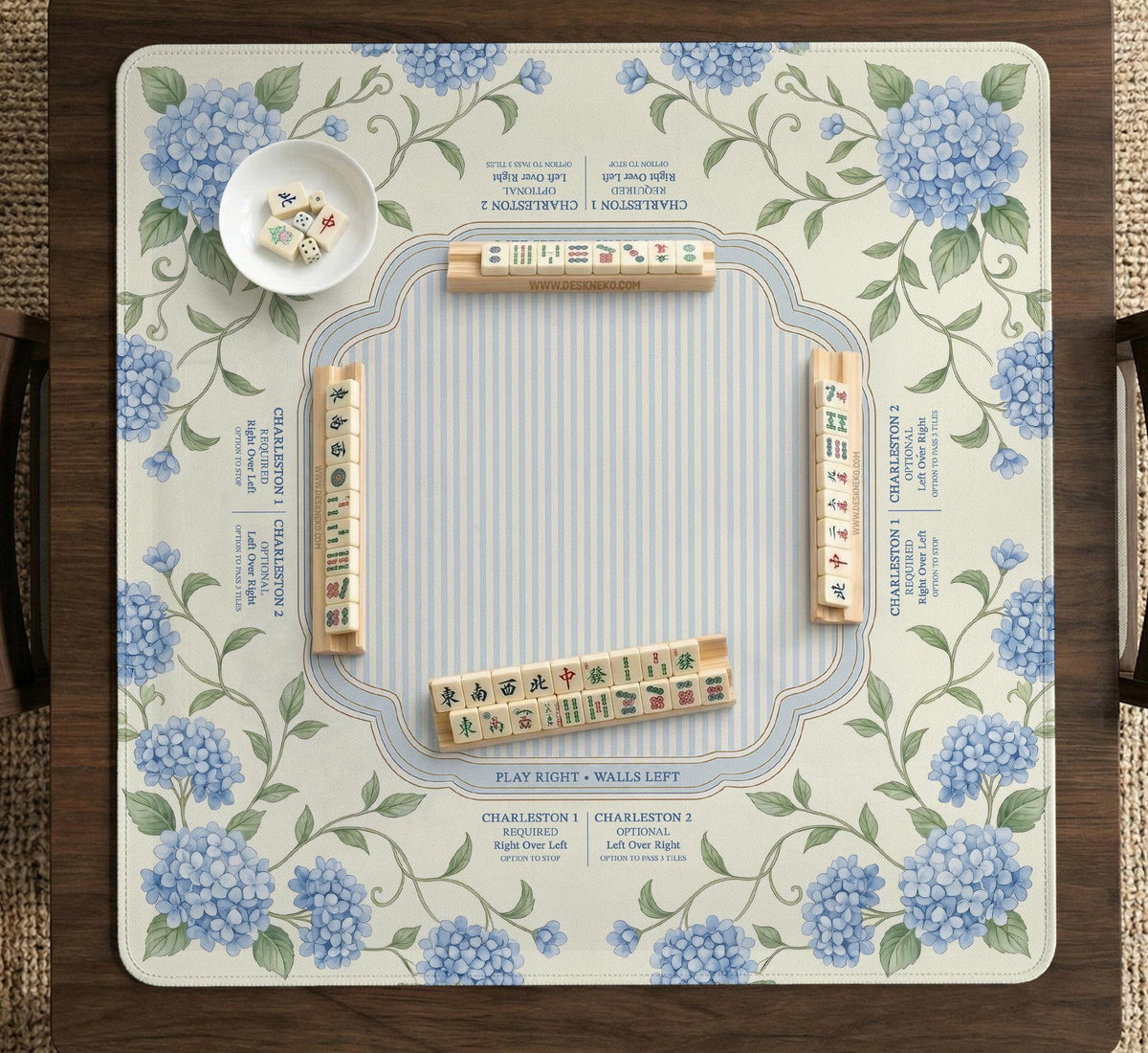 A square mahjong mat with blue hydrangea flowers, green vines, a cream background, a striped center, and printed rules around the border.