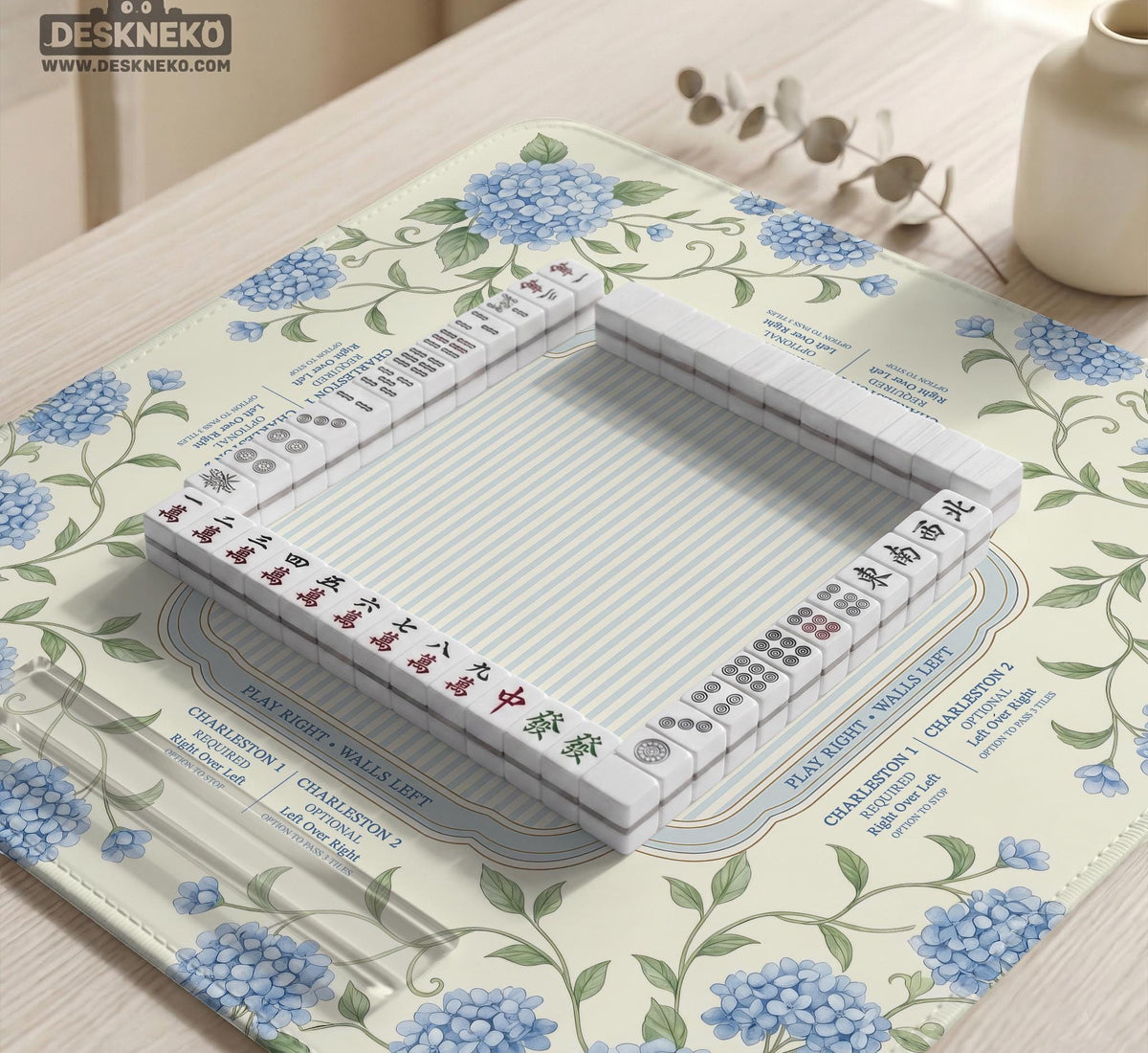 A square mahjong mat with blue hydrangea flowers, green vines, a cream background, a striped center, and printed rules around the border.
