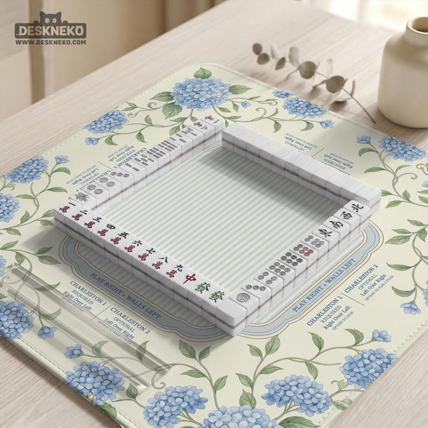 A square mahjong mat with blue hydrangea flowers, green vines, a cream background, a striped center, and printed rules around the border.