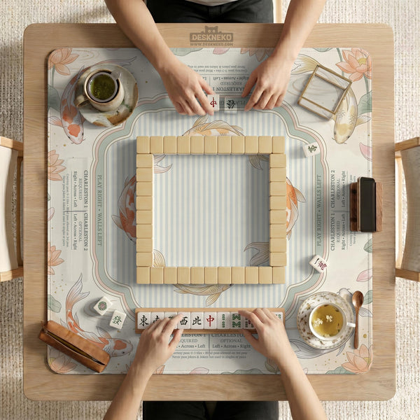 Sage and cream mahjong mat with a koi fish pond pattern, lotus blooms, water ripples, and printed instructions around the border. One version has a scalloped edge.