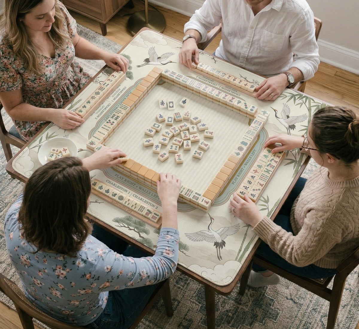 Sage green scalloped mahjong mat with bamboo, crane, and blossom illustration and printed rules around the border.