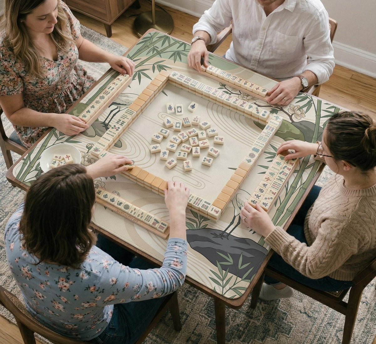 Square mahjong mat with a cream background, sage green cranes, bamboo leaves, peony branches, stones, and thin linework.