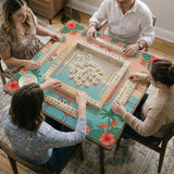 A square mahjong mat with flamingos, hibiscus flowers, palm leaves, and aqua water accents on a coral background with a scalloped edge.