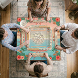 A square mahjong mat with flamingos, hibiscus flowers, palm leaves, and aqua water accents on a coral background with a scalloped edge.