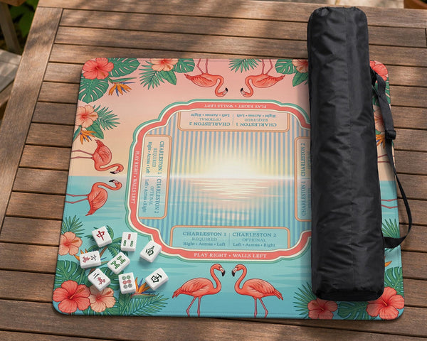 A square mahjong mat with flamingos, hibiscus flowers, palm leaves, and aqua water accents on a coral background with a scalloped edge.