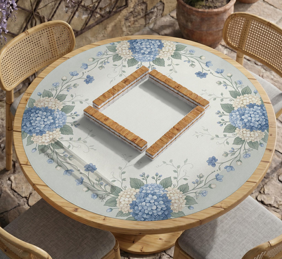 A square blue mahjong mat with hydrangea flowers, cream blossoms, sage leaves, and vines around a plain center play area. The edge is scalloped.