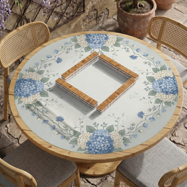 A square blue mahjong mat with hydrangea flowers, cream blossoms, sage leaves, and vines around a plain center play area. The edge is scalloped.