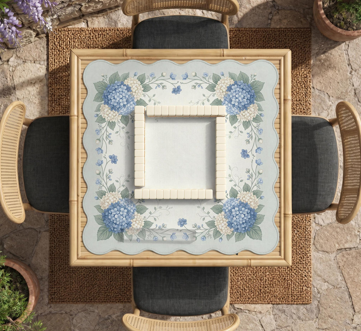 A square blue mahjong mat with hydrangea flowers, cream blossoms, sage leaves, and vines around a plain center play area. The edge is scalloped.