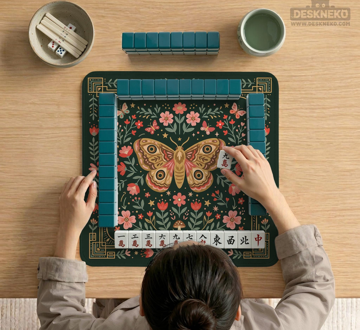 Dark green square mahjong mat with floral branches, small red blossoms, gold line details, and a large moth in the center.
