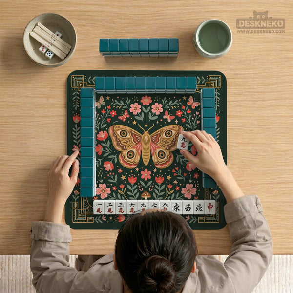 Dark green square mahjong mat with floral branches, small red blossoms, gold line details, and a large moth in the center.
