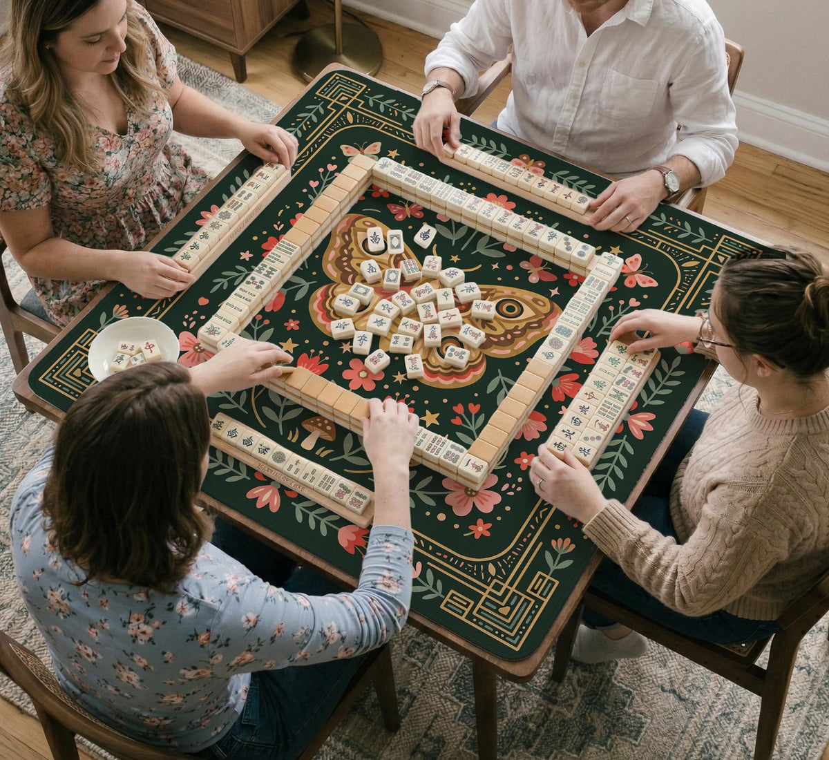 Dark green square mahjong mat with floral branches, small red blossoms, gold line details, and a large moth in the center.
