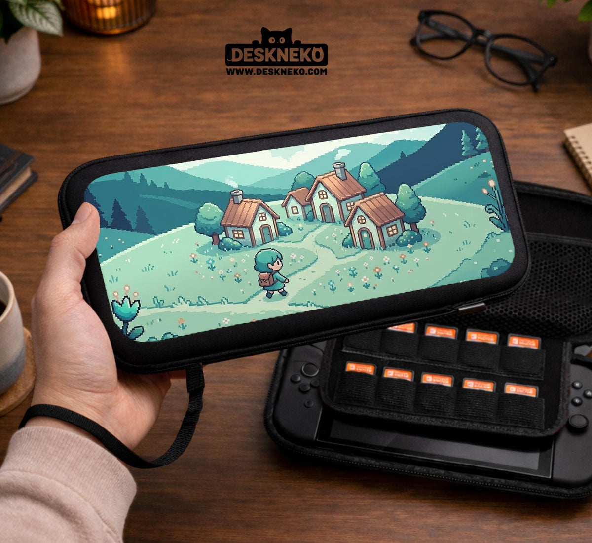 Teal carrying case with a pixel-style village scene, small houses, layered mountains, flowers, and a retro game-inspired landscape design.