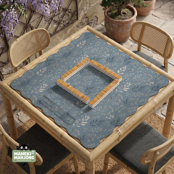 Blue mahjong mat with a botanical floral pattern, pale leaves, and delicate stems on a dusty blue background.