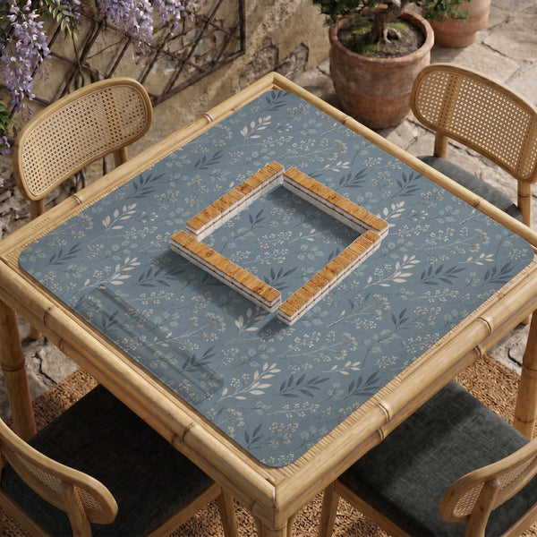 Blue mahjong mat with a botanical floral pattern, pale leaves, and delicate stems on a dusty blue background.