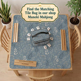 Blue mahjong mat with a botanical floral pattern, pale leaves, and delicate stems on a dusty blue background.