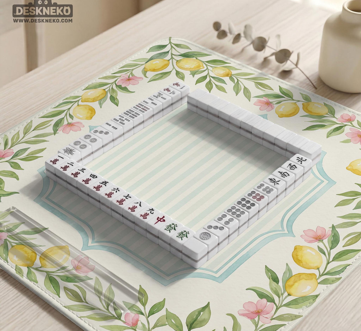 Square yellow mahjong mat with a citrus garden border, green vines, pink blossoms, aqua accents, and a plain center play area.