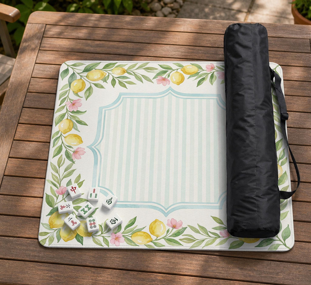 Square yellow mahjong mat with a citrus garden border, green vines, pink blossoms, aqua accents, and a plain center play area.