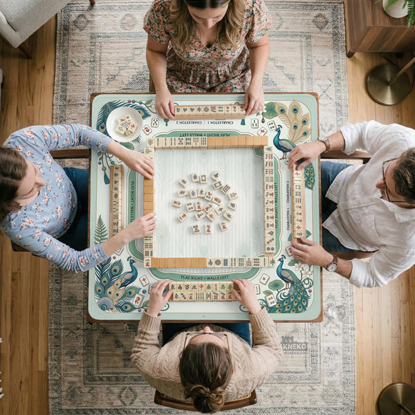Teal square mahjong mat with peacock feathers, soft floral pattern, tassel details, and printed rule guide text in the center.