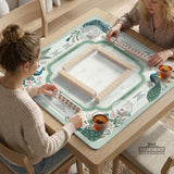 Teal square mahjong mat with peacock feathers, soft floral pattern, tassel details, and printed rule guide text in the center.