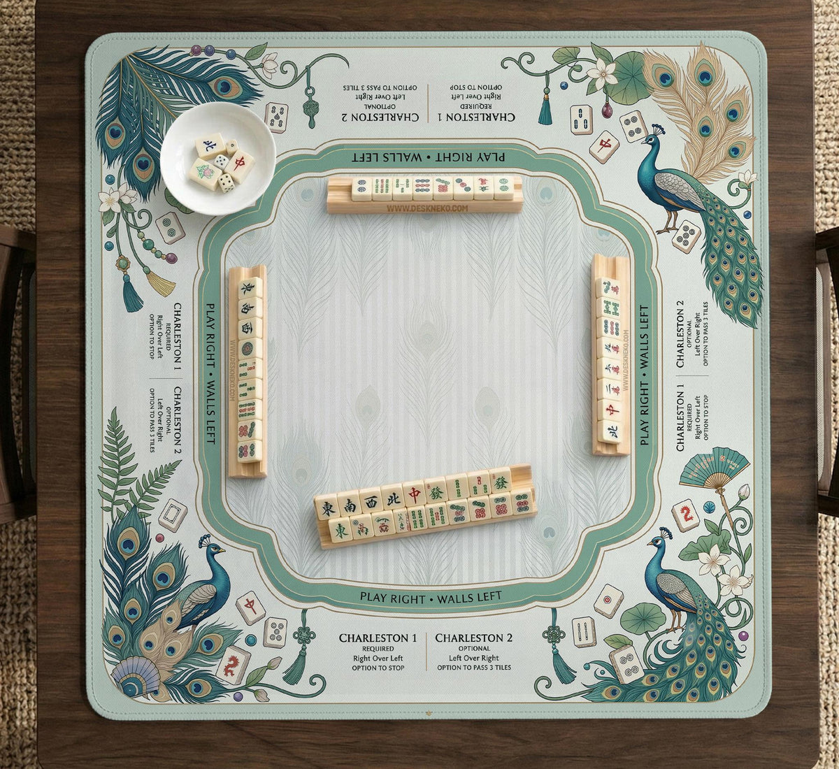 Teal square mahjong mat with peacock feathers, soft floral pattern, tassel details, and printed rule guide text in the center.
