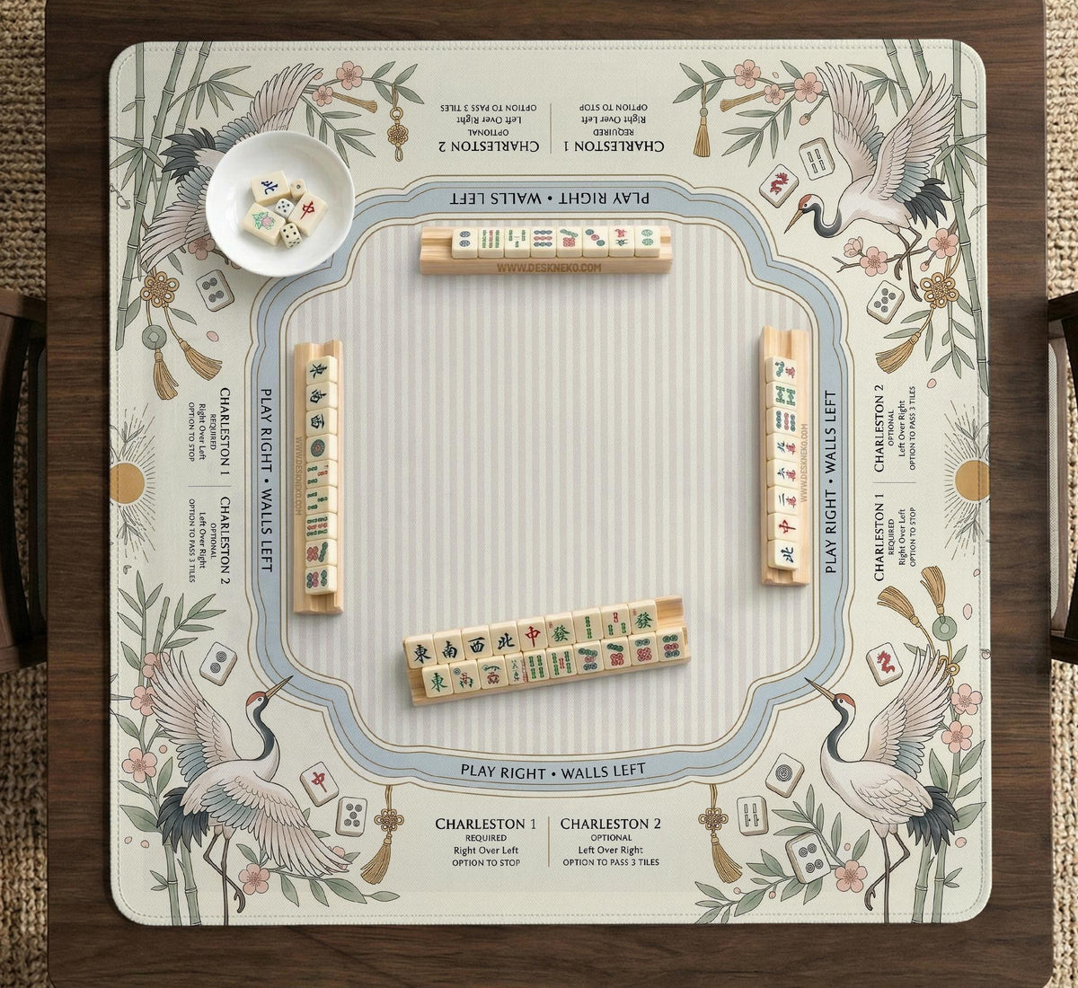 Beige square mahjong mat with a sage border, crane birds, bamboo, flowers, tile icons, and printed rules around a clean center play area.