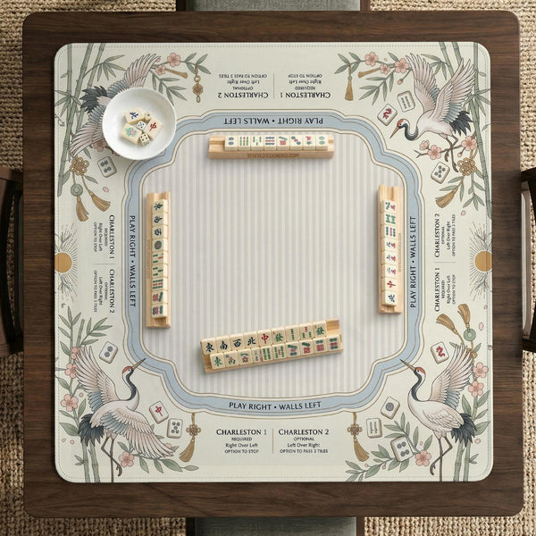 Beige square mahjong mat with a sage border, crane birds, bamboo, flowers, tile icons, and printed rules around a clean center play area.