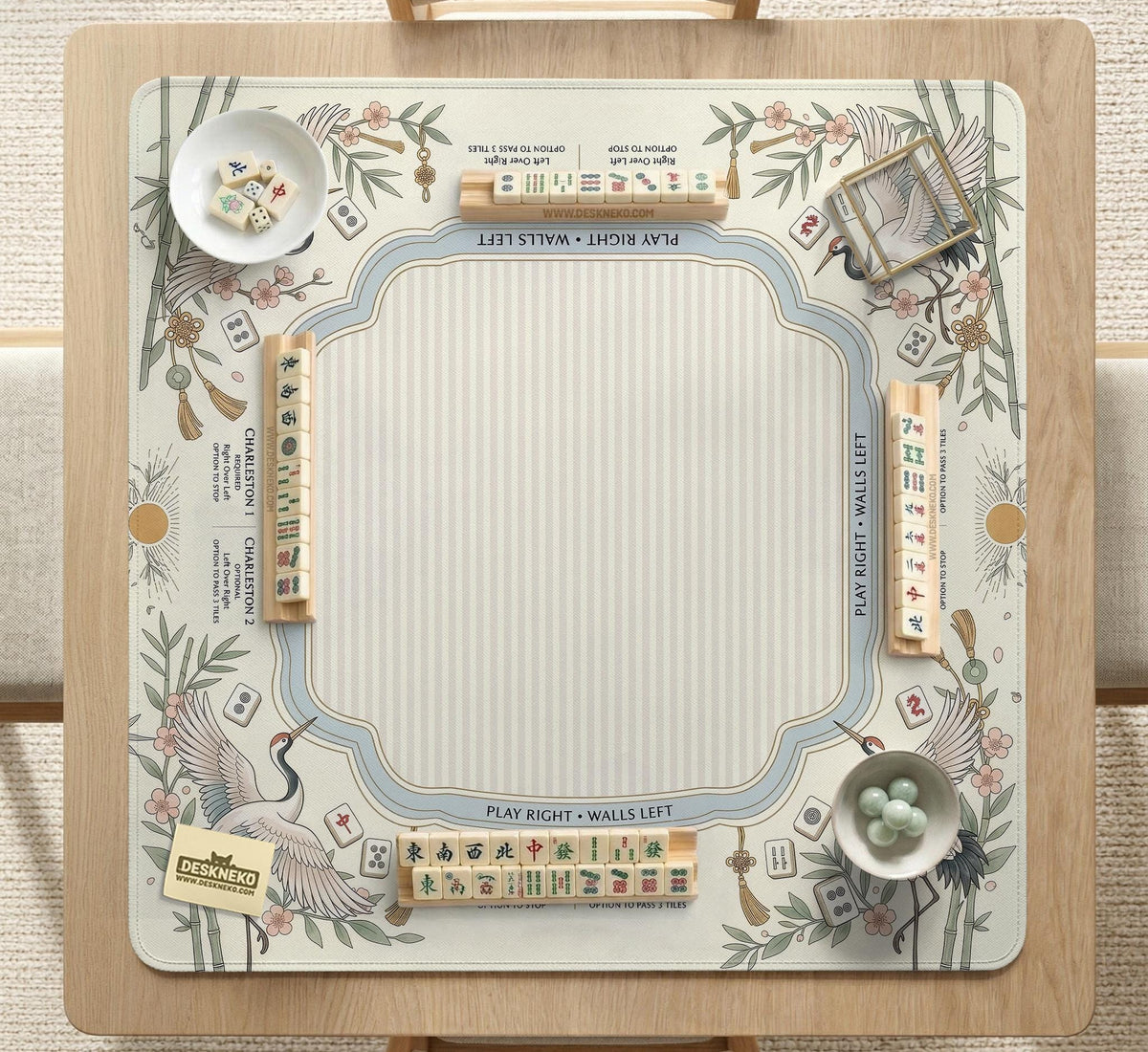 Beige square mahjong mat with a sage border, crane birds, bamboo, flowers, tile icons, and printed rules around a clean center play area.