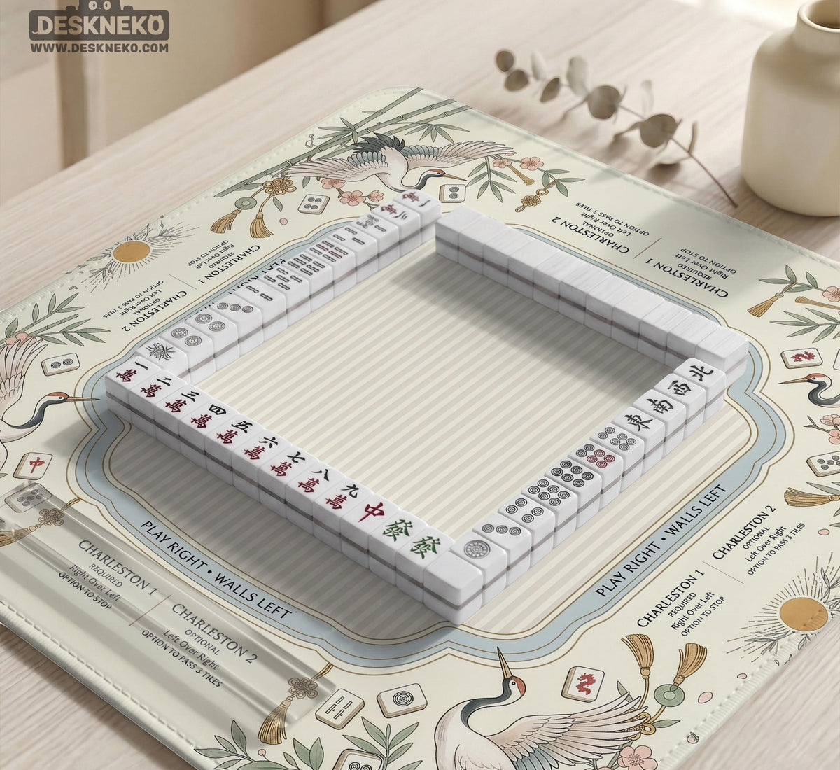 Beige square mahjong mat with a sage border, crane birds, bamboo, flowers, tile icons, and printed rules around a clean center play area.