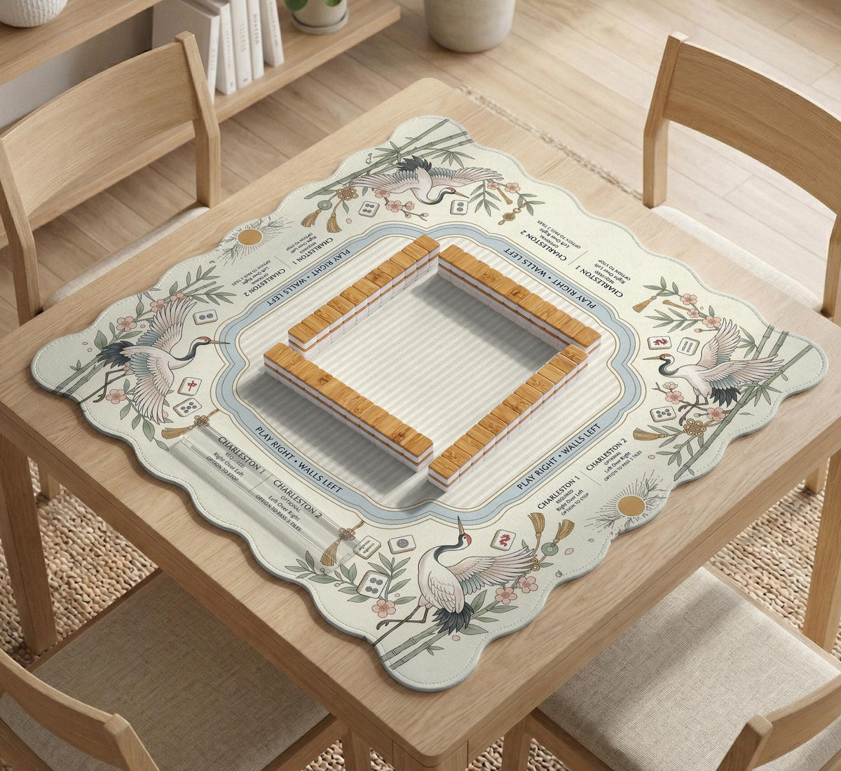 Beige square mahjong mat with a sage border, crane birds, bamboo, flowers, tile icons, and printed rules around a clean center play area.