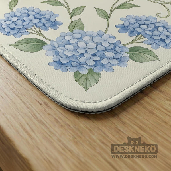A square mahjong mat with blue hydrangea flowers, green vines, a cream background, a striped center, and printed rules around the border.