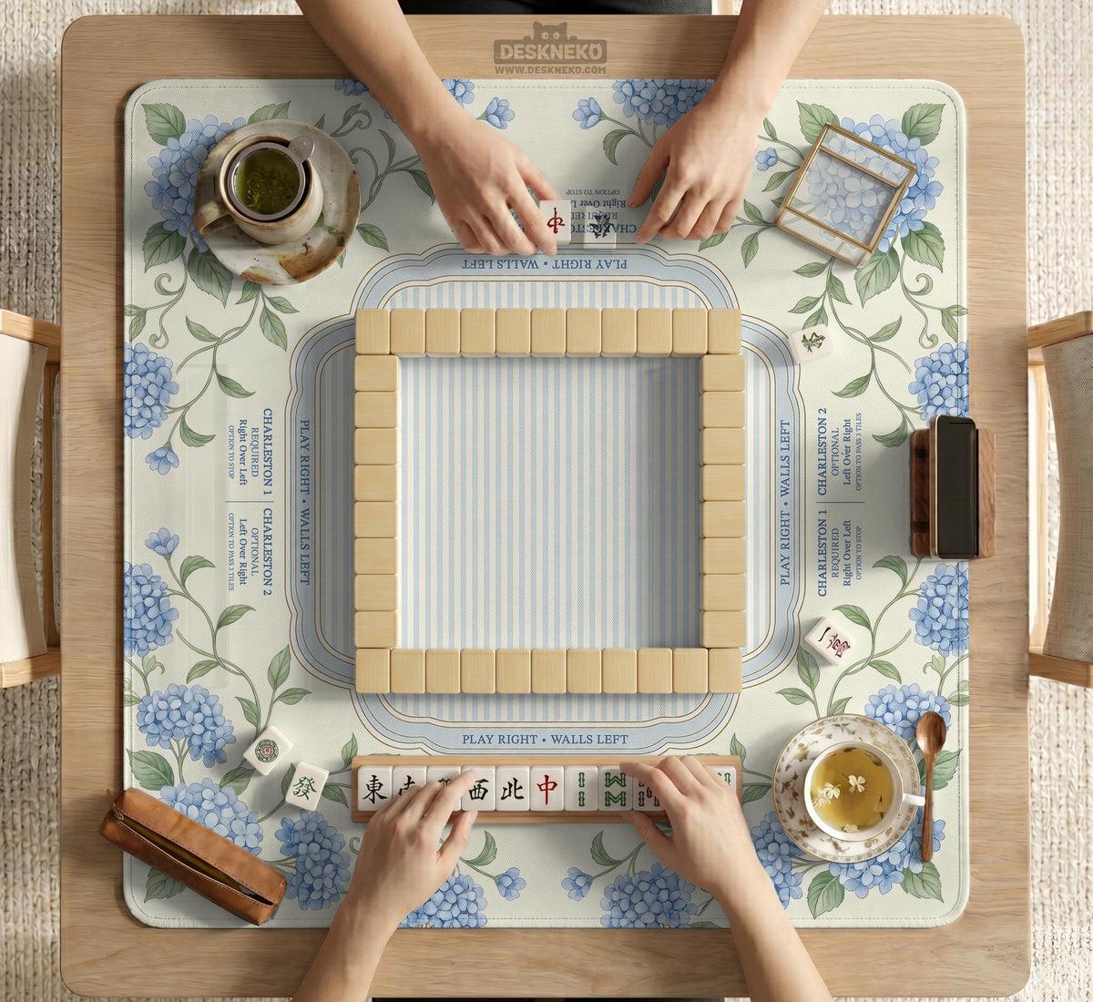 A square mahjong mat with blue hydrangea flowers, green vines, a cream background, a striped center, and printed rules around the border.