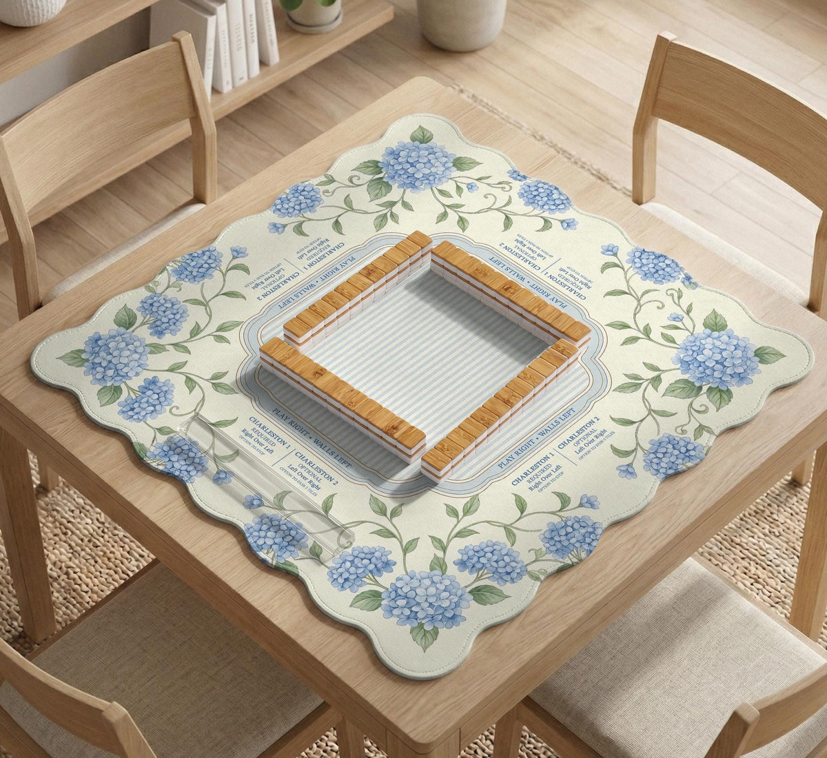 A square mahjong mat with blue hydrangea flowers, green vines, a cream background, a striped center, and printed rules around the border.