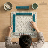 Cream mahjong mat with a floral pattern of small wildflowers and sage leaves, shown with a scalloped edge on a light neutral background.
