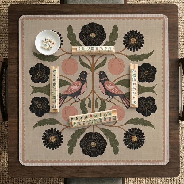Beige mahjong mat with a botanical floral bird design, blush flowers, olive green leaves, black flower accents, and a warm linen-style background. Scalloped edge option shown.