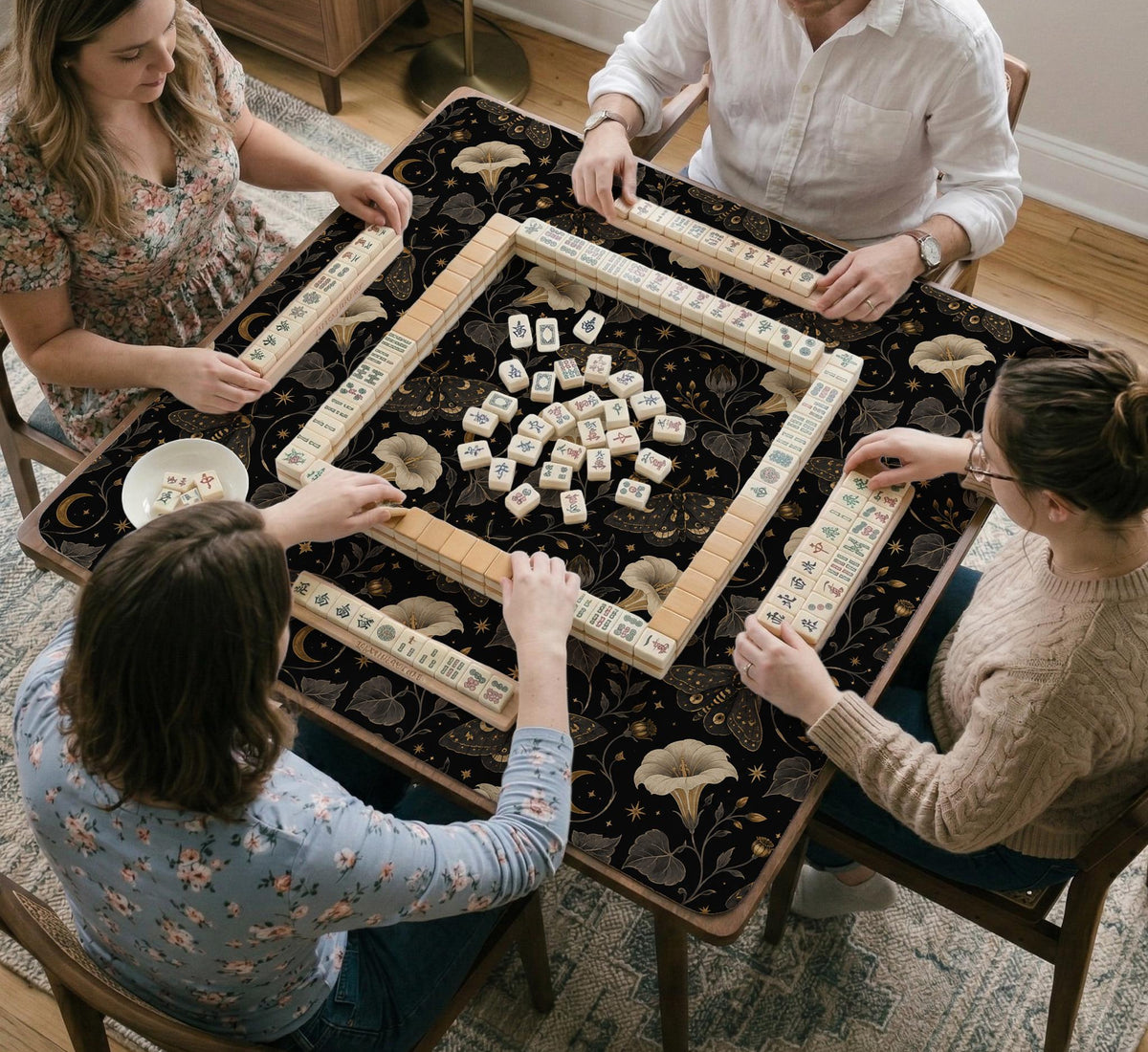 Black square mahjong mat with moths, moonflowers, crescent moons, and scattered stars in a celestial floral pattern.