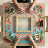 A square mahjong mat with flamingos, hibiscus flowers, palm leaves, and aqua water accents on a coral background with a scalloped edge.
