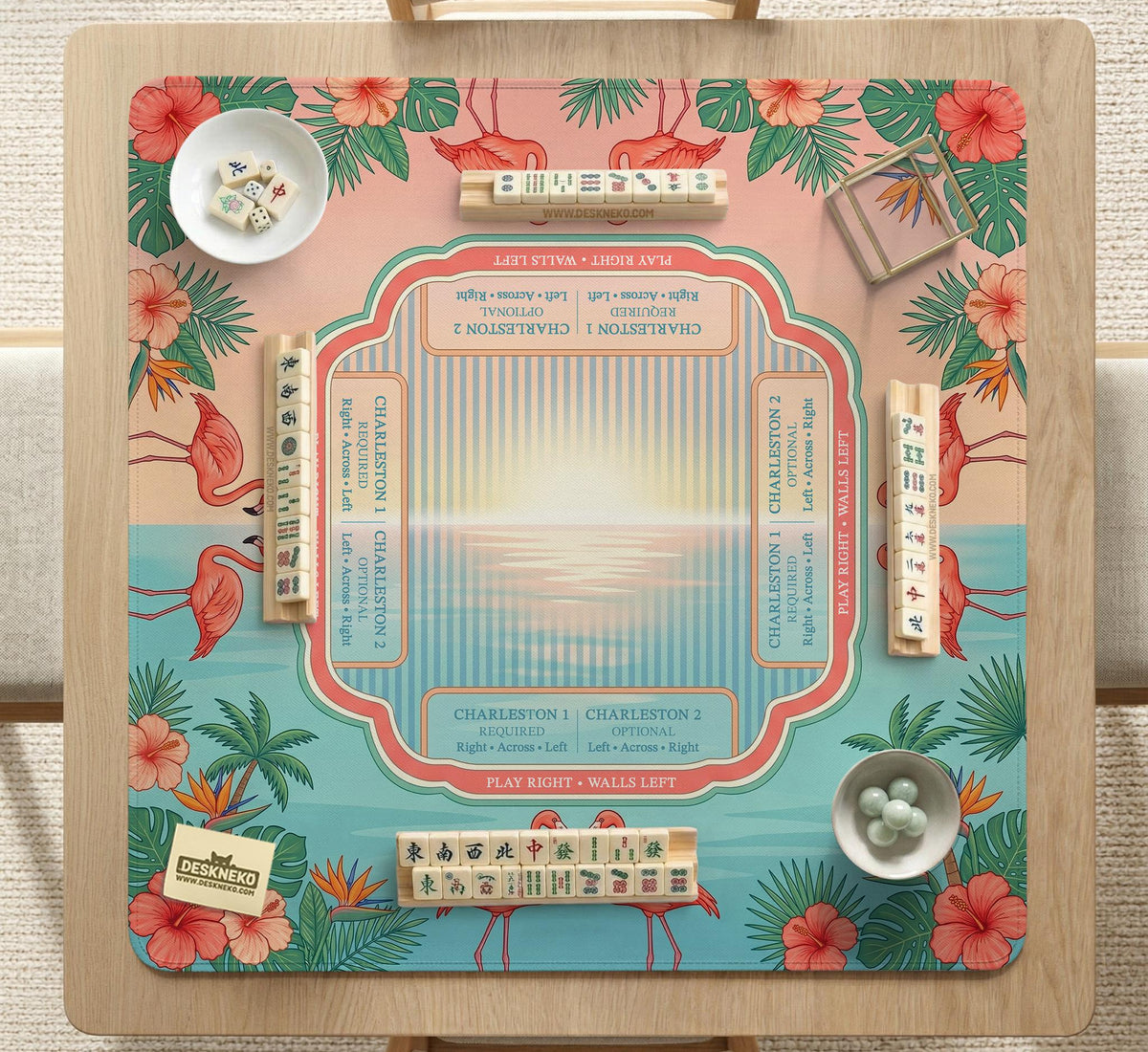 A square mahjong mat with flamingos, hibiscus flowers, palm leaves, and aqua water accents on a coral background with a scalloped edge.
