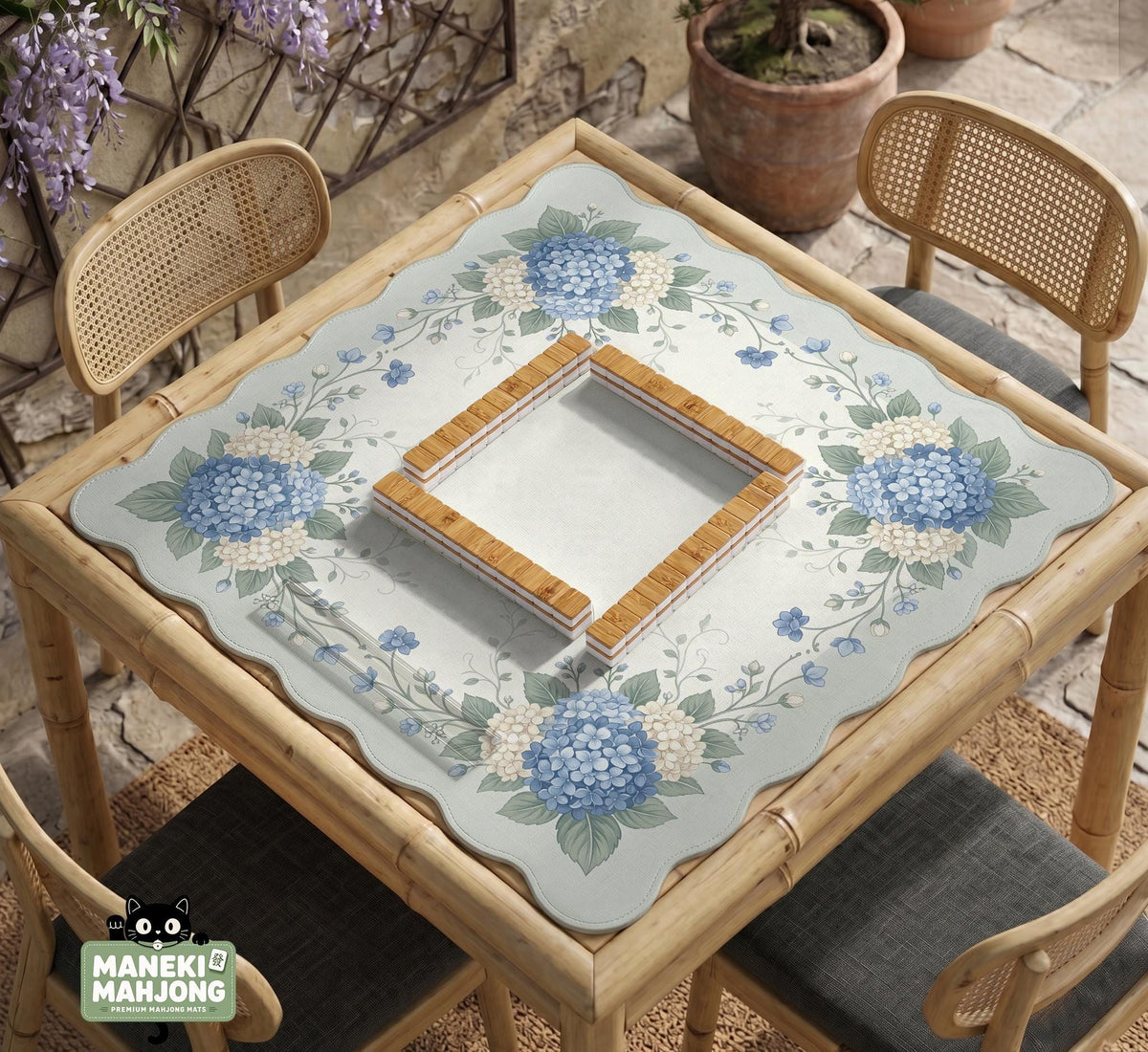 A square blue mahjong mat with hydrangea flowers, cream blossoms, sage leaves, and vines around a plain center play area. The edge is scalloped.