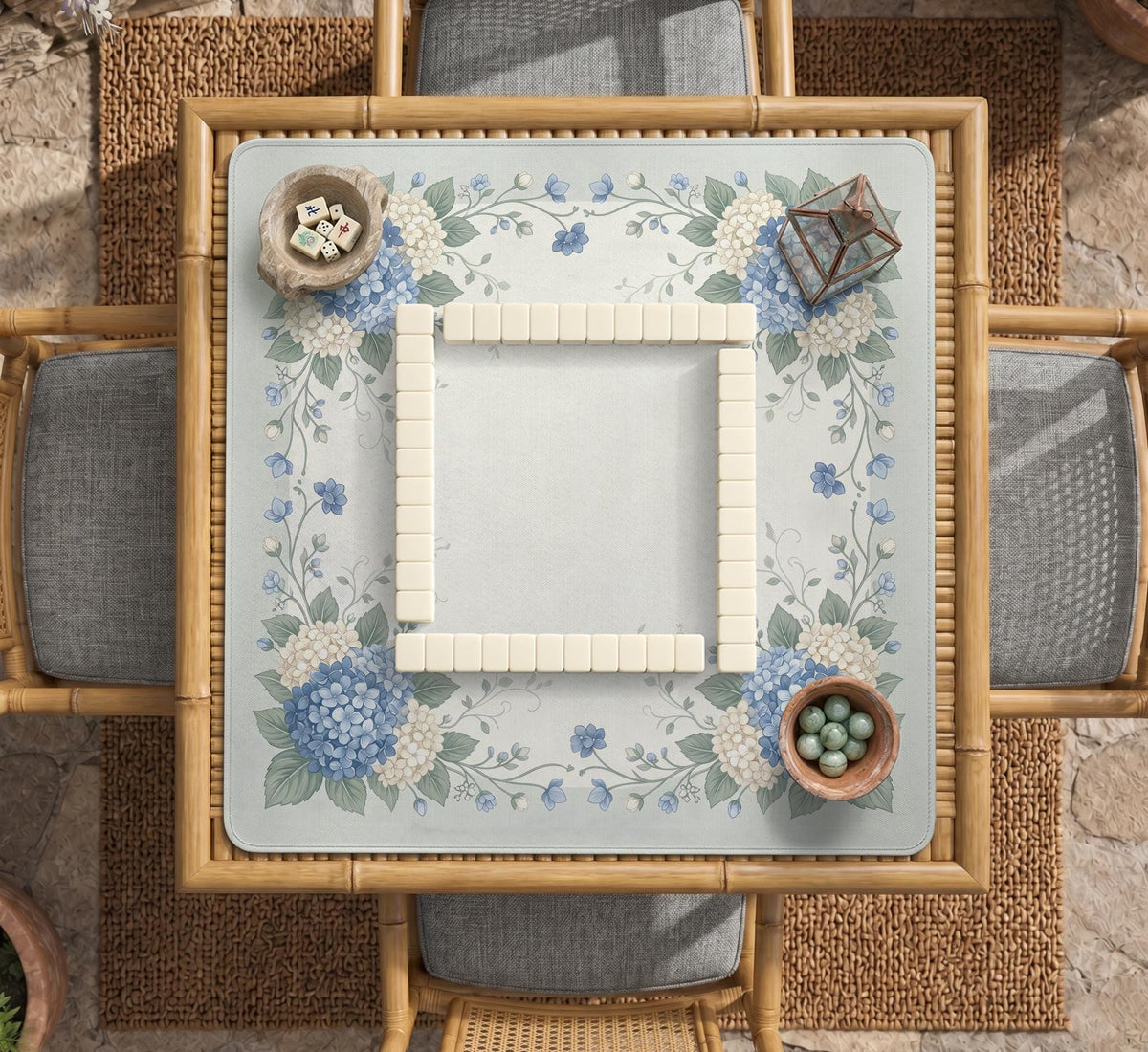 A square blue mahjong mat with hydrangea flowers, cream blossoms, sage leaves, and vines around a plain center play area. The edge is scalloped.