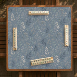 Blue mahjong mat with a botanical floral pattern, pale leaves, and delicate stems on a dusty blue background.